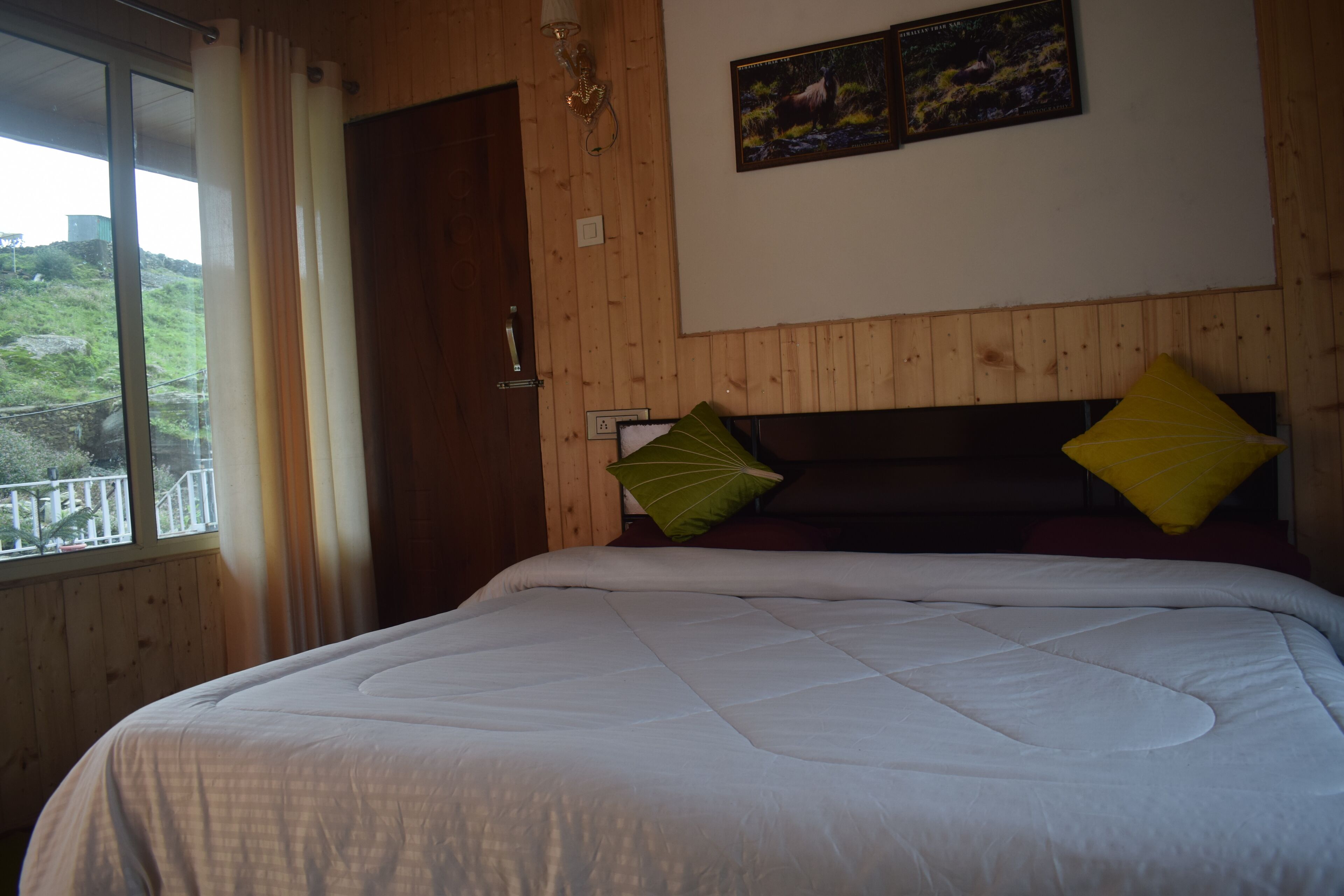 A bedroom with a large bed, wooden walls, a window with curtains, and a painting on the wall.