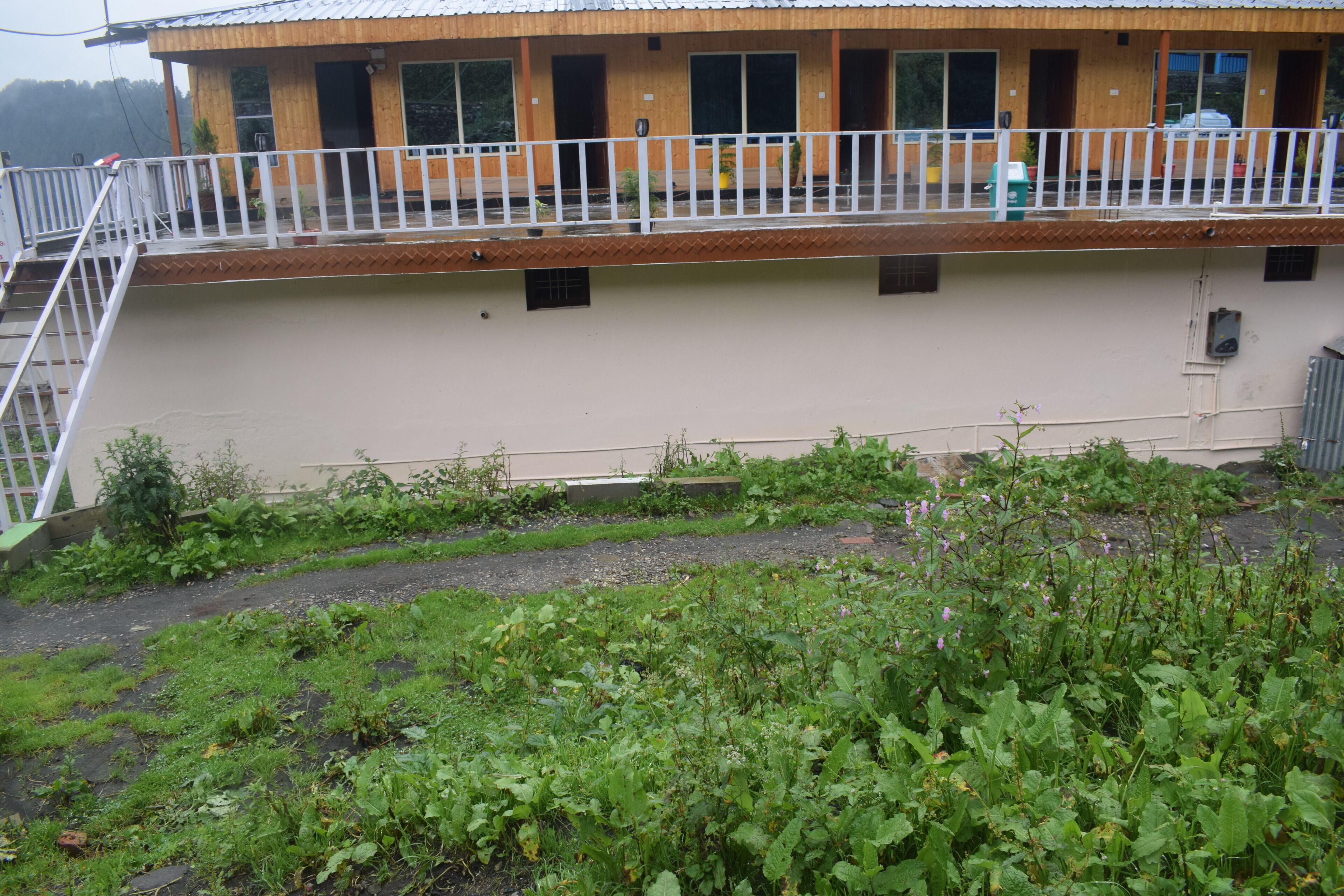 Un edificio de dos pisos con un balcón, una terraza de madera y un jardín delantero.