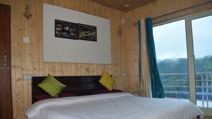 A wooden-paneled bedroom with a large bed, two pillows, a framed picture on the wall, and a window with curtains. - Chopta Himrab Resort  (Pokhri)