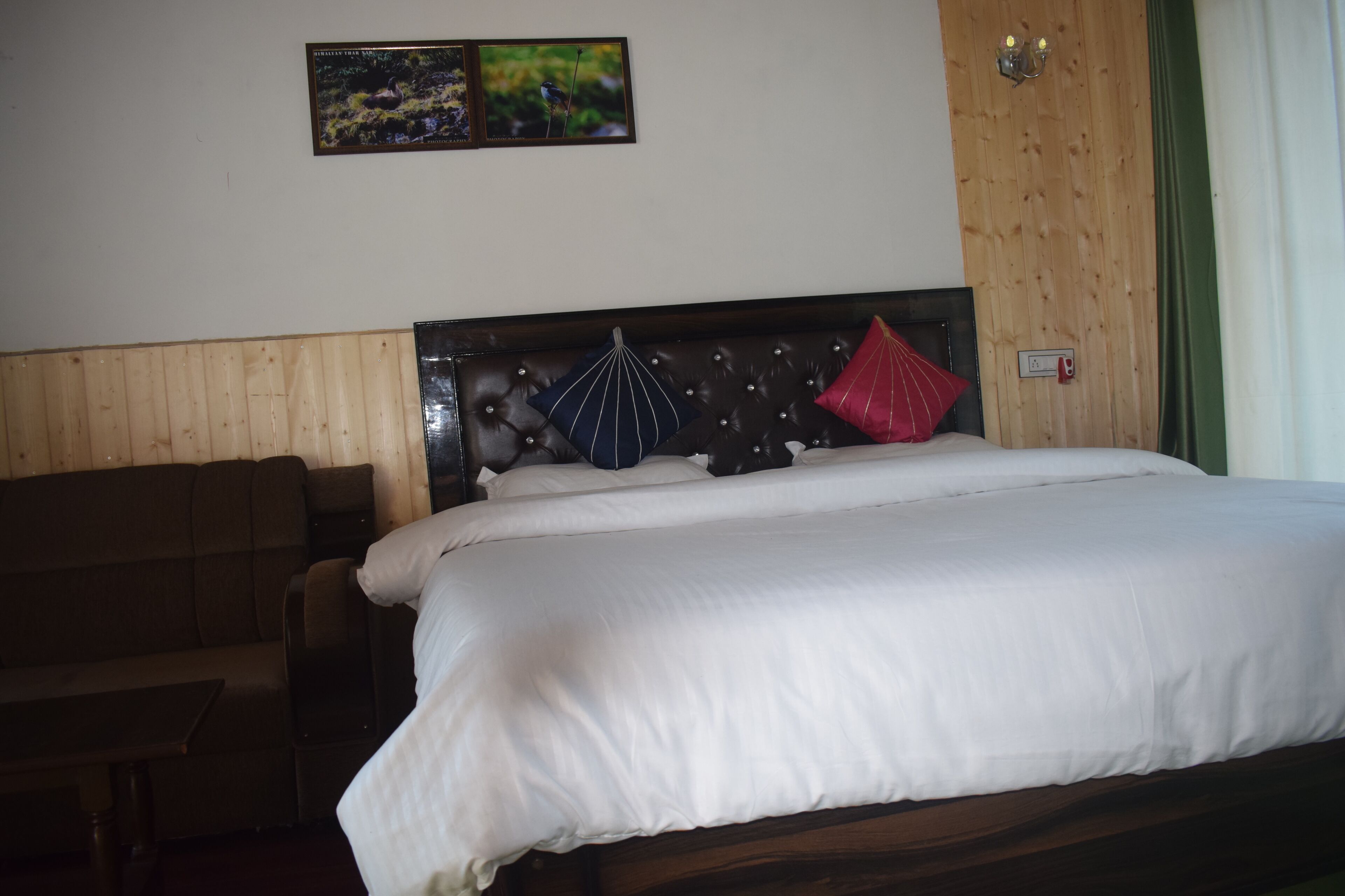 Una habitación de hotel con cabecera de madera, cama con ropa de cama blanca, sofá marrón y dos cuadros en la pared.