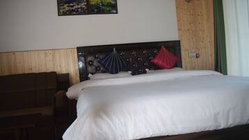 Una habitación de hotel con cabecera de madera, cama con ropa de cama blanca, sofá marrón y dos cuadros en la pared.