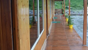 A wooden covered porch with large windows and potted plants. - Chopta Himrab Resort  (Pokhri)