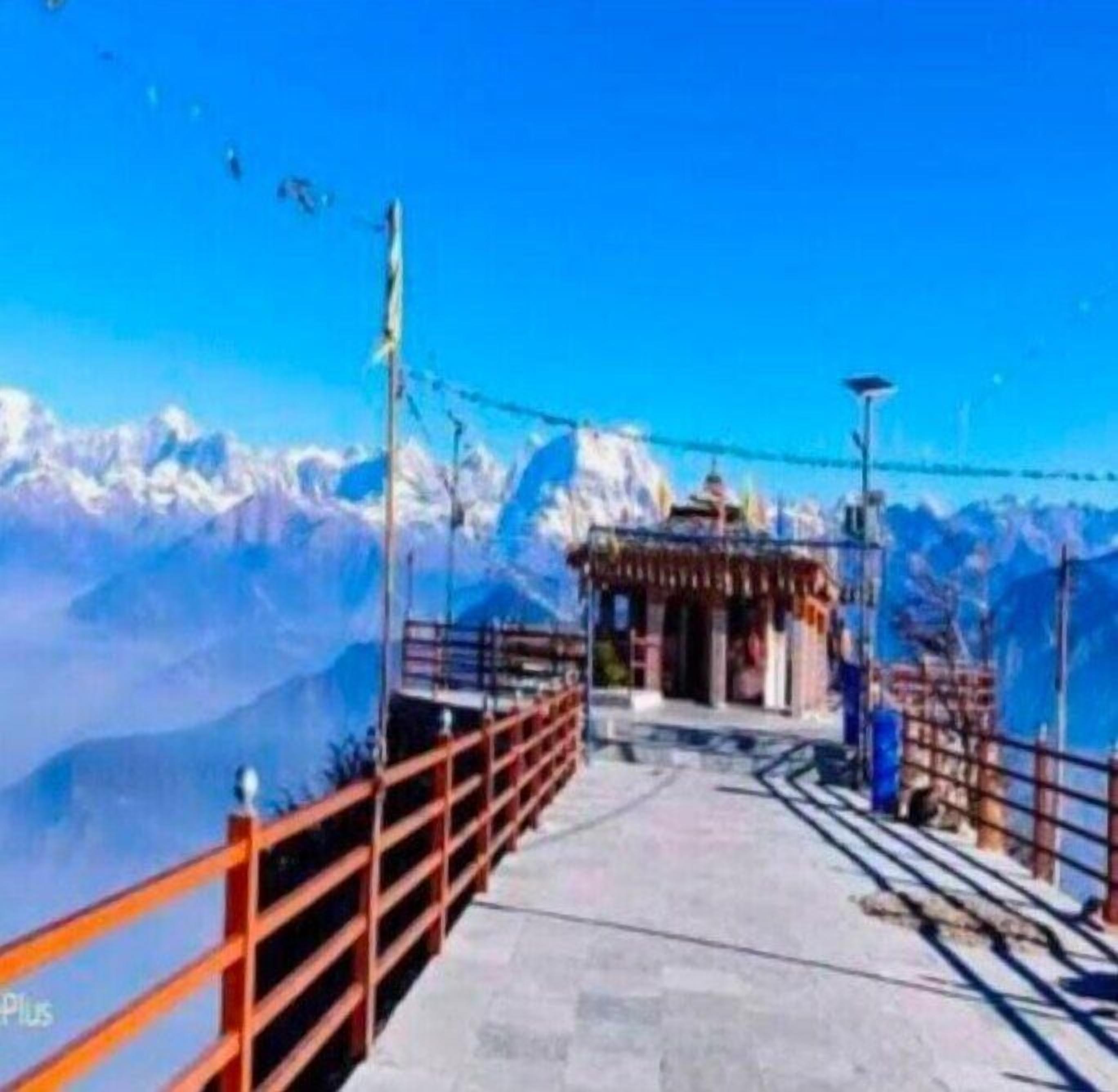 A mountain path leading to a small shrine with a clear view of snow-capped mountains in the background.
