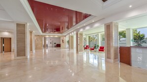 A spacious lobby with a high ceiling, polished marble floors, and red seating areas. - Front Line Beach 2-Bed Apartment with Sea Views, Wi-Fi, and Air Conditioning (Marbella)