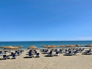 A beach with rows of sun loungers and thatched umbrellas.