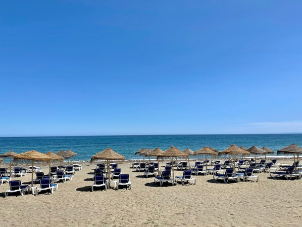 A beach with rows of sun loungers and thatched umbrellas.