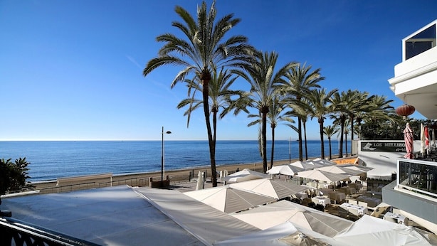 A seaside terrace with white umbrellas, palm trees, and a view of the ocean. - Front Line Beach 2-Bed Apartment with Sea Views, Wi-Fi, and Air Conditioning (Marbella)