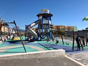 A playground with slides and swings, a water feature, and buildings in the background. - Villa 'By The Beach 5 Bedrooms' with Sea View, Wi-Fi and Air Conditioning (Marbella)