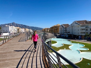 A pedestrian bridge with a unique curved design, a fountain area, and buildings in the background.