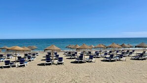 Une plage bordée de rangées de chaises longues et d’ombrelles en chaume.