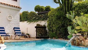 Une piscine entourée de chaises longues, d’une pergola et d’une végétation luxuriante.