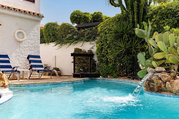 Une piscine entourée de chaises longues, d’une pergola et d’une végétation luxuriante.