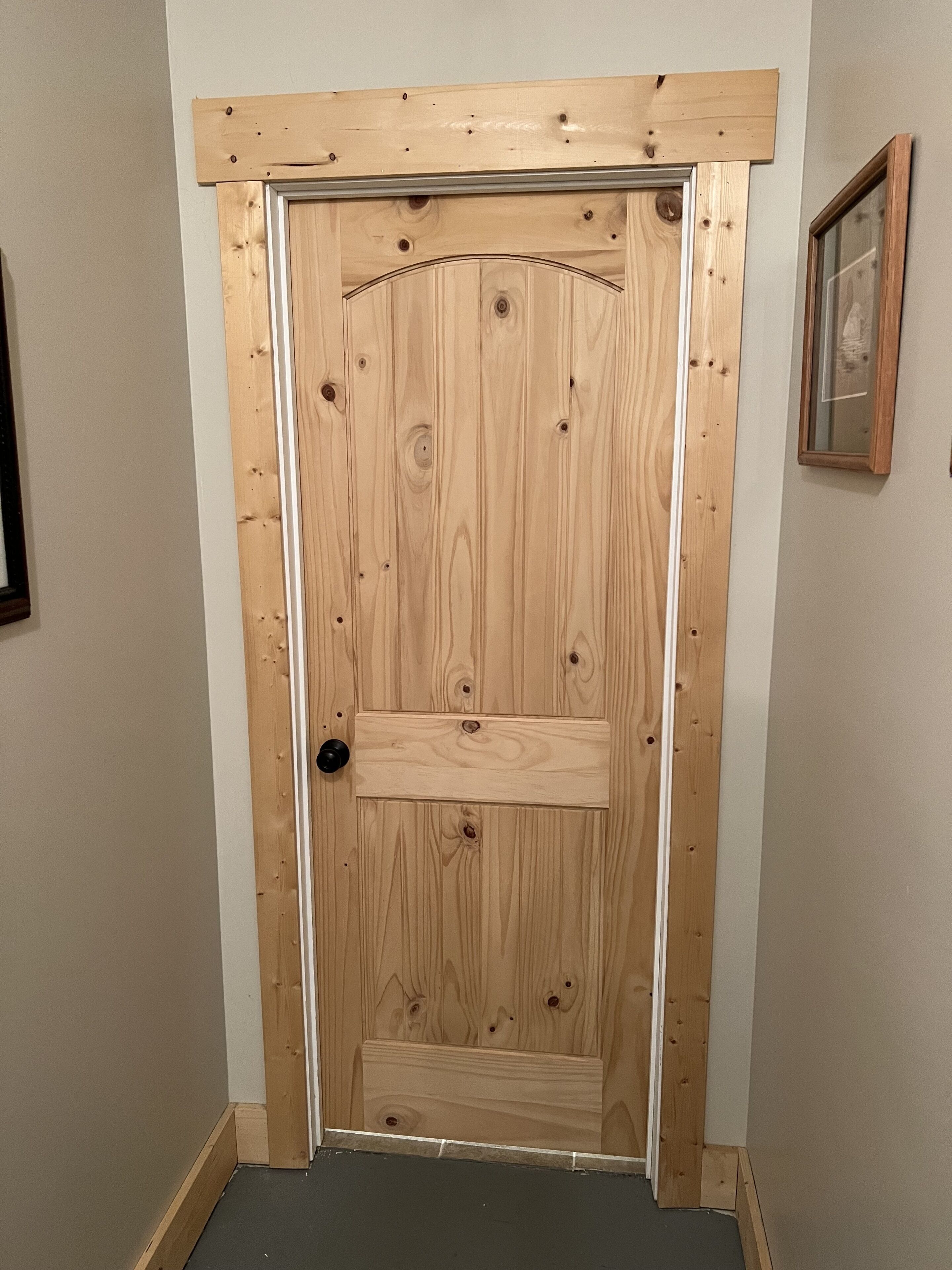 Uma porta de madeira com design simples, um pequeno degrau na base e uma maçaneta preta.