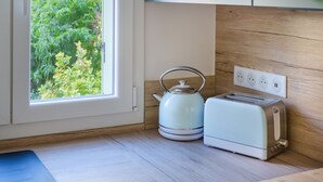 A kitchen with a window, a kettle, a toaster, and a wooden wall. - Holiday Home 'Jolie Maison' with Wi-Fi (Lucéram)