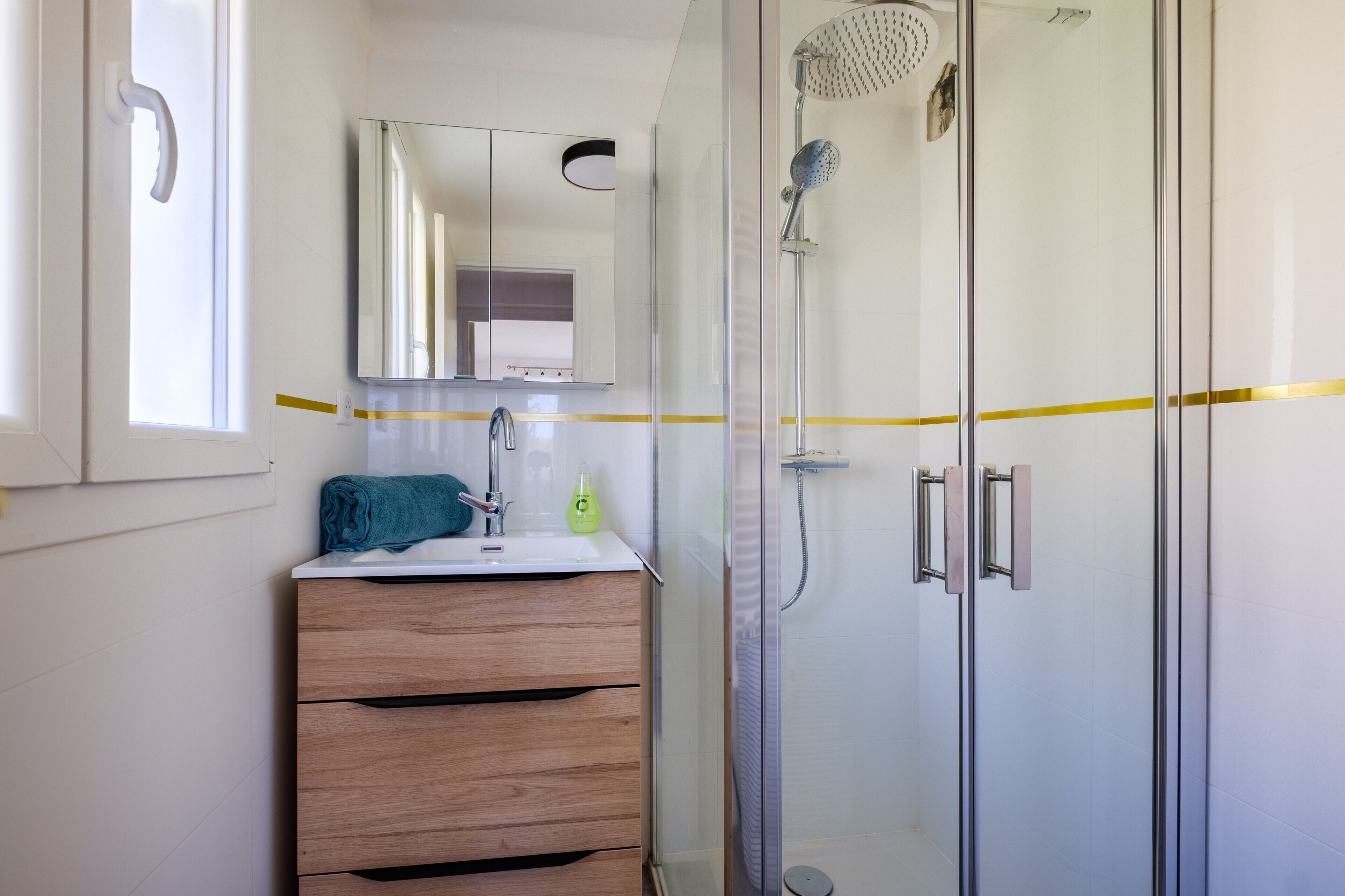 Un baño con cabina de ducha de vidrio, tocador de madera, espejo y ventana.