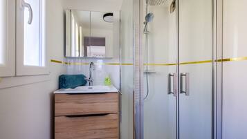 Un baño con cabina de ducha de vidrio, tocador de madera, espejo y ventana.