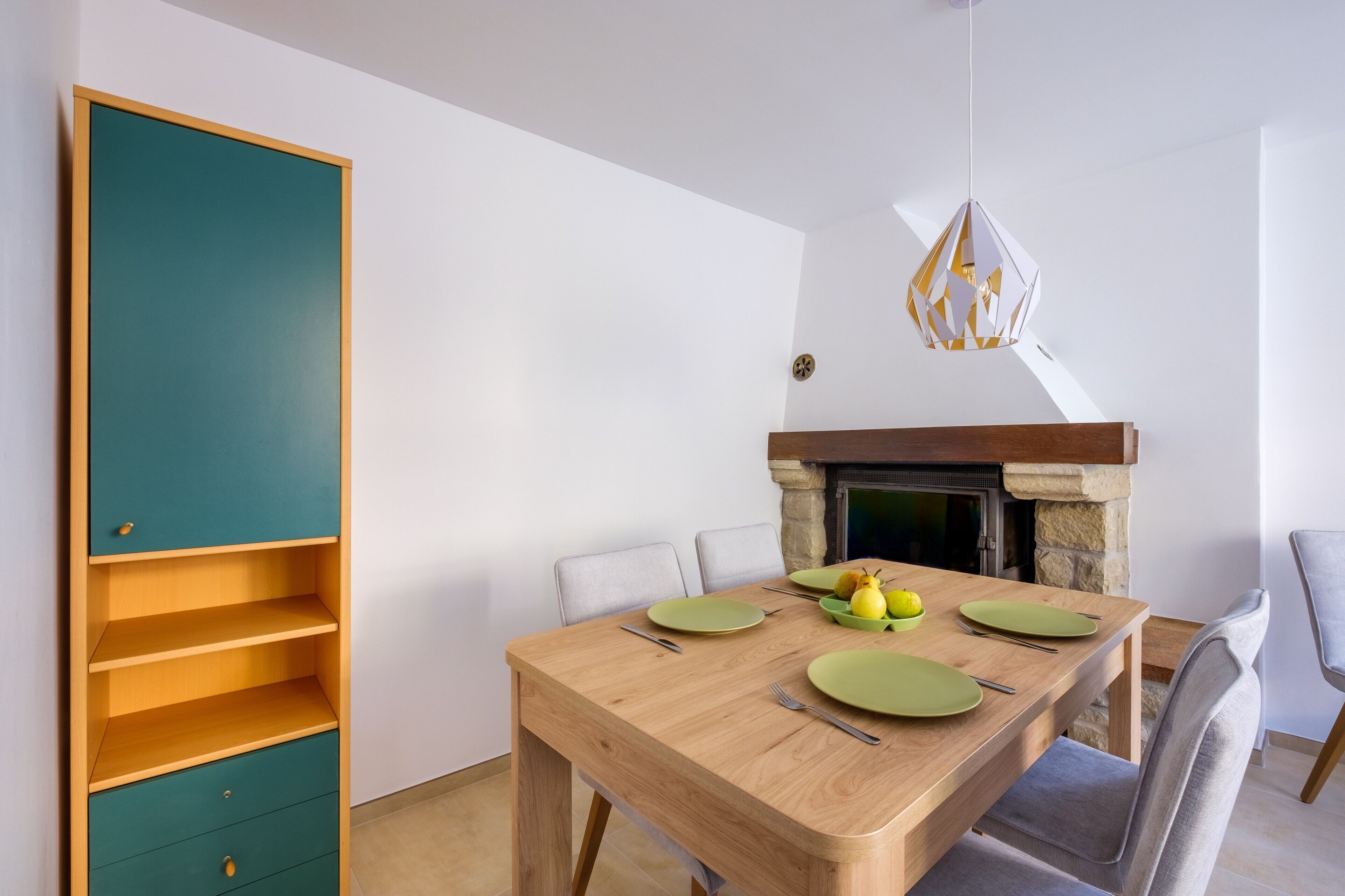 Een eetgedeelte met een houten tafel, groene borden en een schaal met fruit.