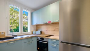 A modern kitchen with light blue cabinets, a stainless steel refrigerator, a built-in oven, and a window with a view of greenery. - Holiday Home 'Jolie Maison' with Wi-Fi (Lucéram)
