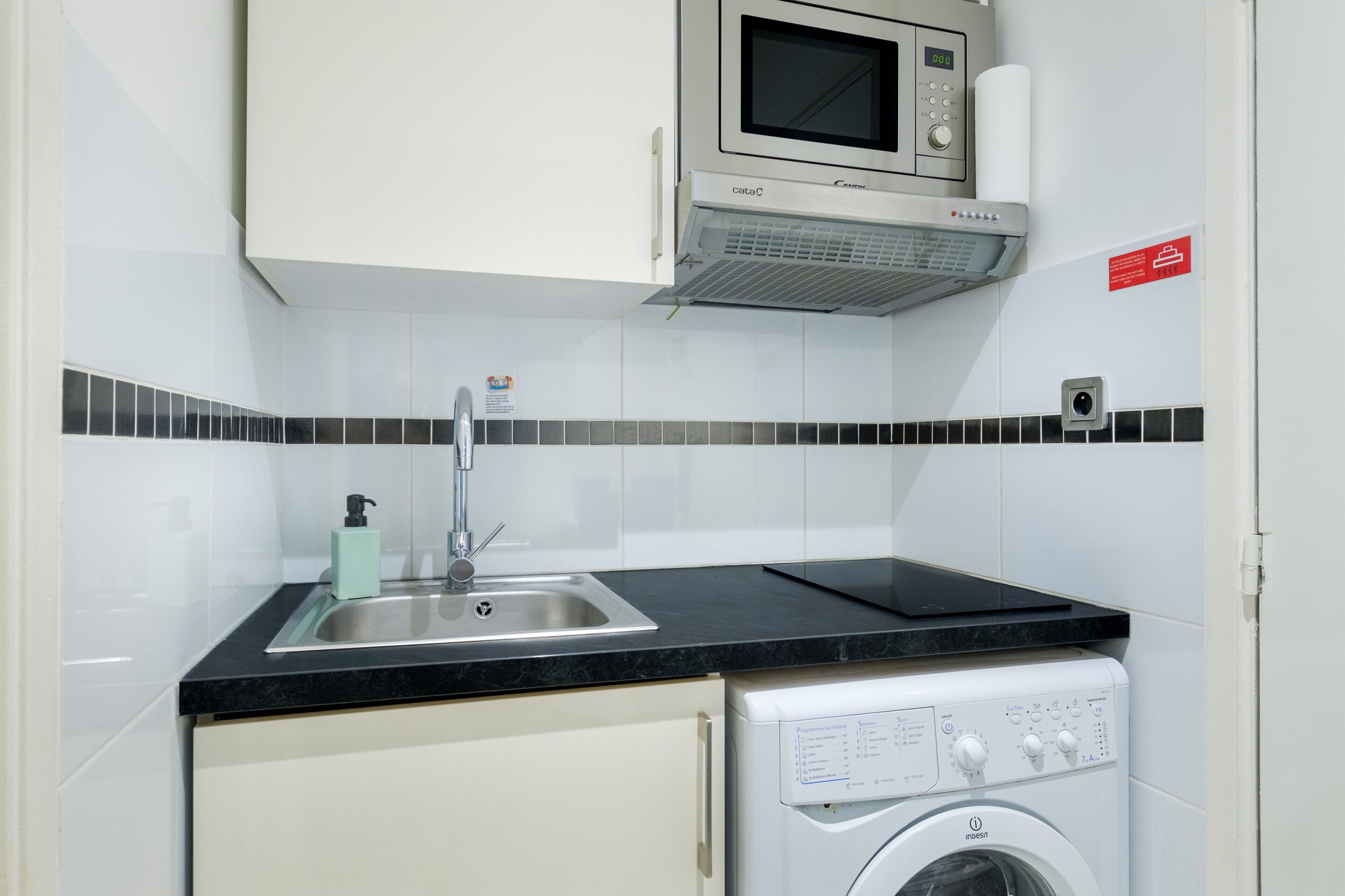 Een kleine keuken met een magnetron, spoelbak en wasmachine.