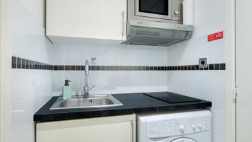 Een kleine keuken met een magnetron, spoelbak en wasmachine.