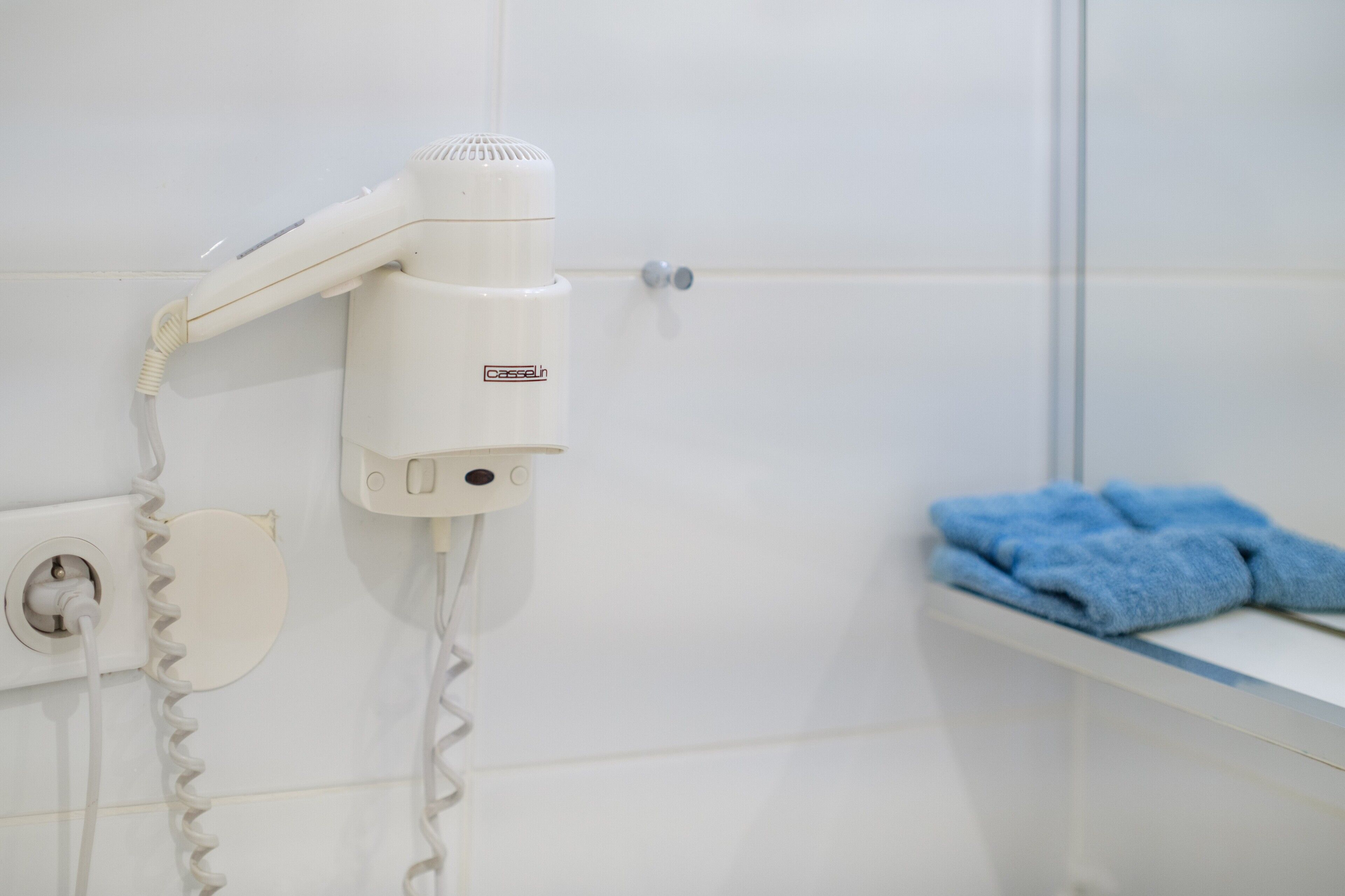 Un sèche-cheveux fixé au mur, un porte-serviettes avec une serviette et une prise de courant.