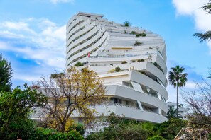 Un edificio moderno de varios pisos con balcones curvos, rodeado de vegetación.