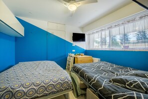 Una habitación con dos camas, ventilador de techo, televisión y ventana con cortinas.