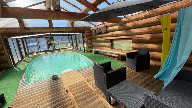 A wooden cabin with a pool, wicker furniture, and a large umbrella.