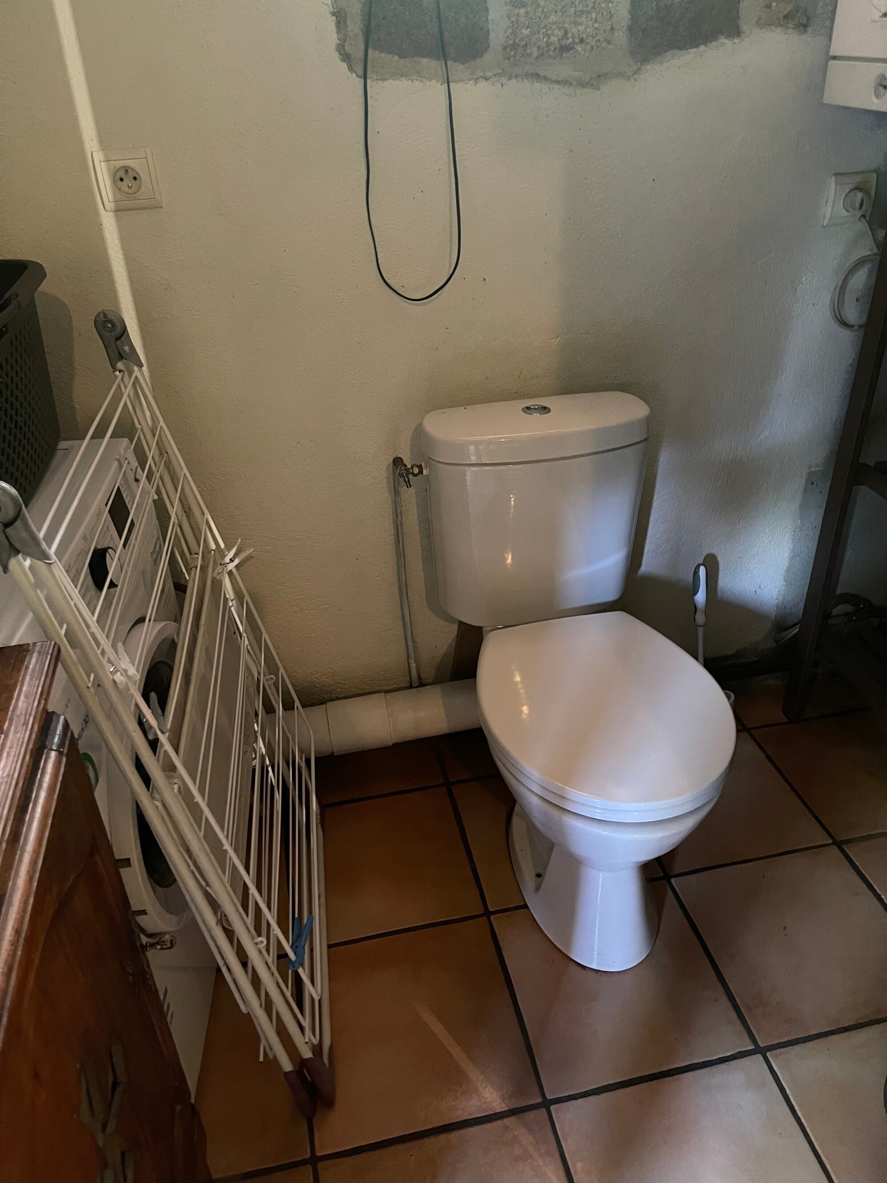 Un bagno con il water bianco, una mensola in metallo e un pavimento piastrellato.