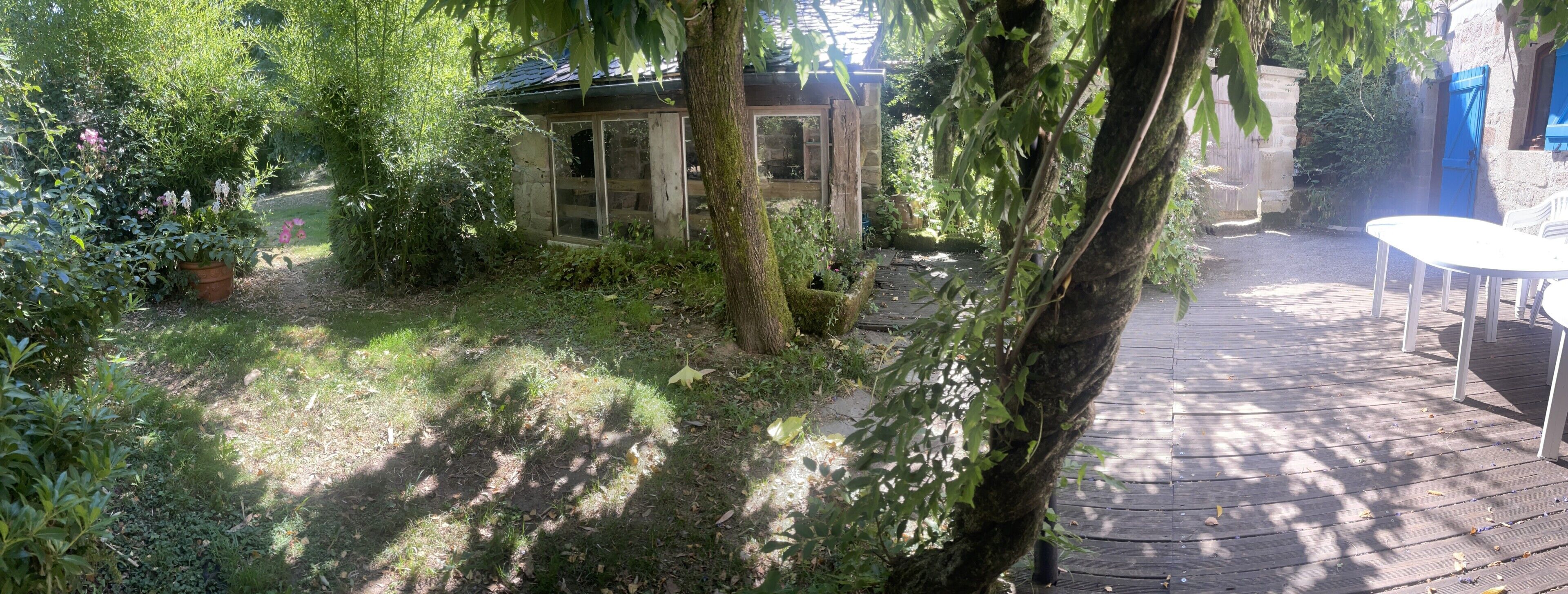 Un jardin agrémenté d’une structure en pierre, d’une terrasse en bois et d’une table blanche.