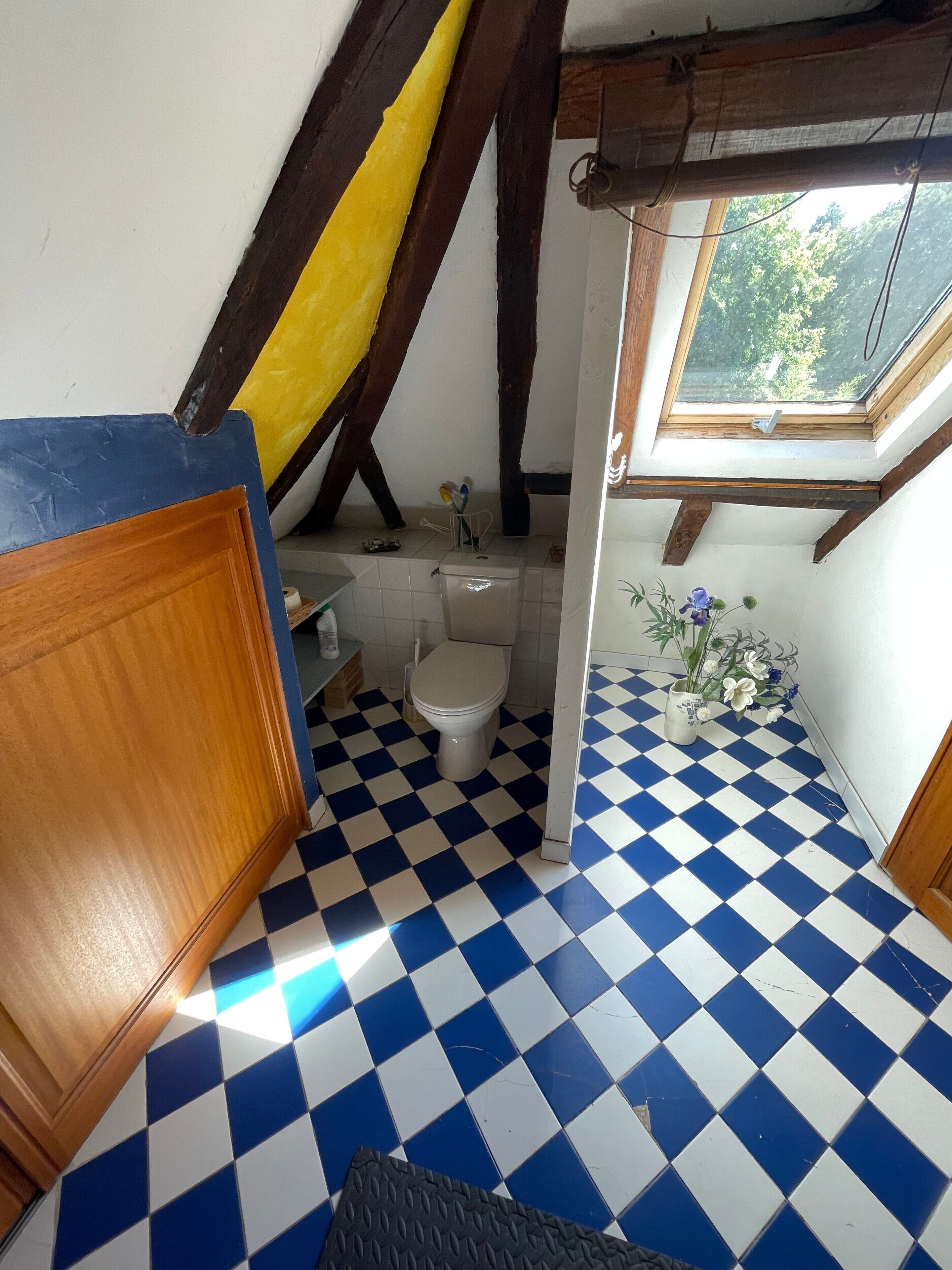 Un bagno con pavimento a scacchi, un water, un lavandino e una finestra vista alberi.