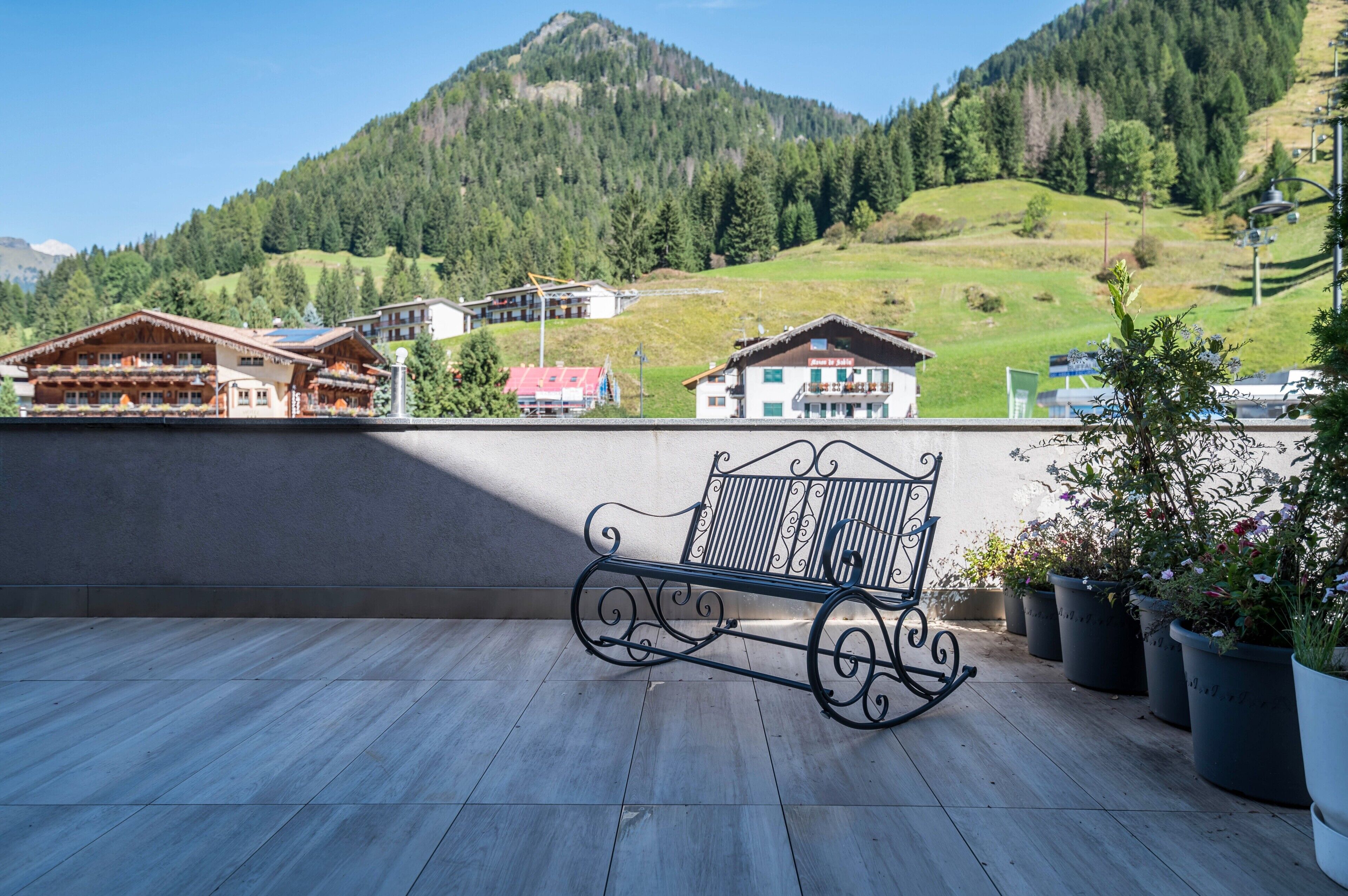 Un balcon avec un banc en métal, des plantes en pot et une vue sur les maisons de montagne.