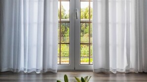 A room with a large window, white curtains, and a floral arrangement on the windowsill. - Holiday Home "Sweet Home Madeira" with Sea View, Private Terrace & Wi-Fi (Camacha)