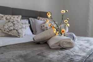 Un lit bien fait, agrémenté d’oreillers à motifs, d’une serviette roulée et d’un vase rempli de fleurs jaunes.