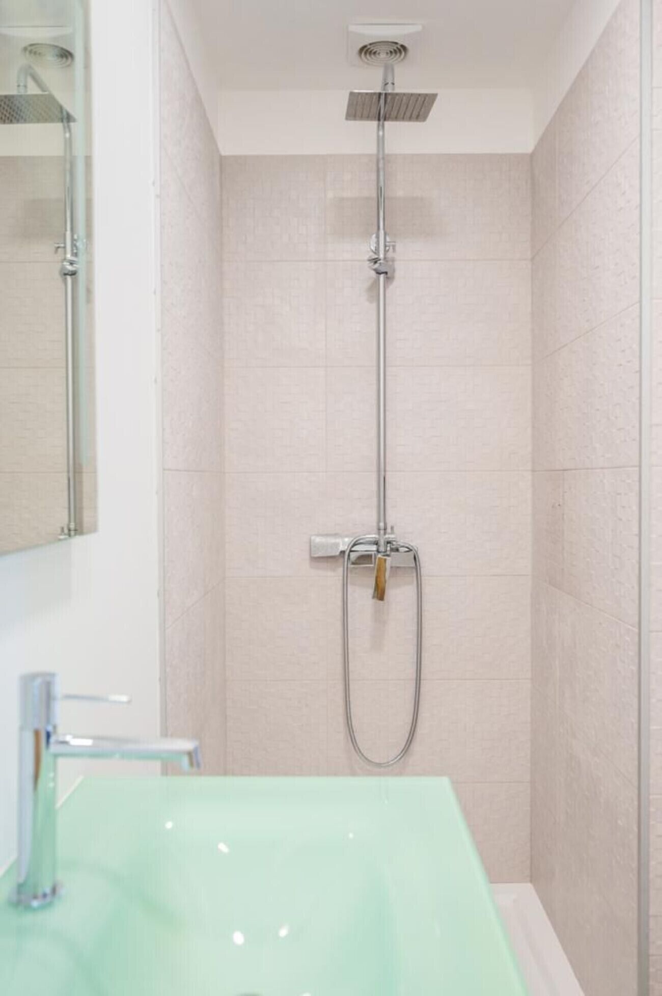 Een badkamer met een glazen wastafel, een douche met een handdouche en een spiegel.
