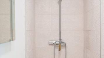 Een badkamer met een glazen wastafel, een douche met een handdouche en een spiegel.