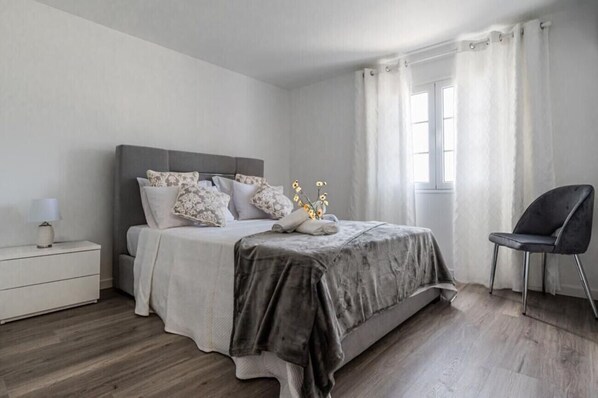 Une chambre à coucher avec un lit, une table de chevet, une chaise et une fenêtre avec des rideaux.