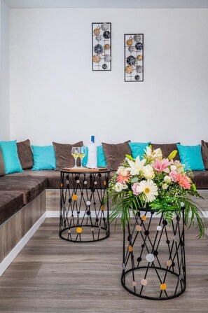 Una sala moderna con un sofá modular, dos mesas auxiliares de metal negro con detalles decorativos, un jarrón de flores y dos obras de arte enmarcadas en la pared.