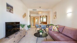 Een moderne woonkamer met een flatscreen televisie, een bank, een eettafel met stoelen en een keuken in de achtergrond.