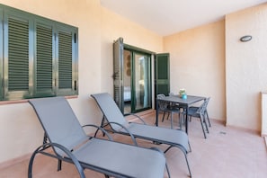 A balcony with two lounge chairs, a small table with chairs, and a door with green shutters. - Holiday Apartment "El Oasis Malasia 16 Bajo A" with Shared Pool, Private Terrace & Wi-Fi (Fuente Álamo)