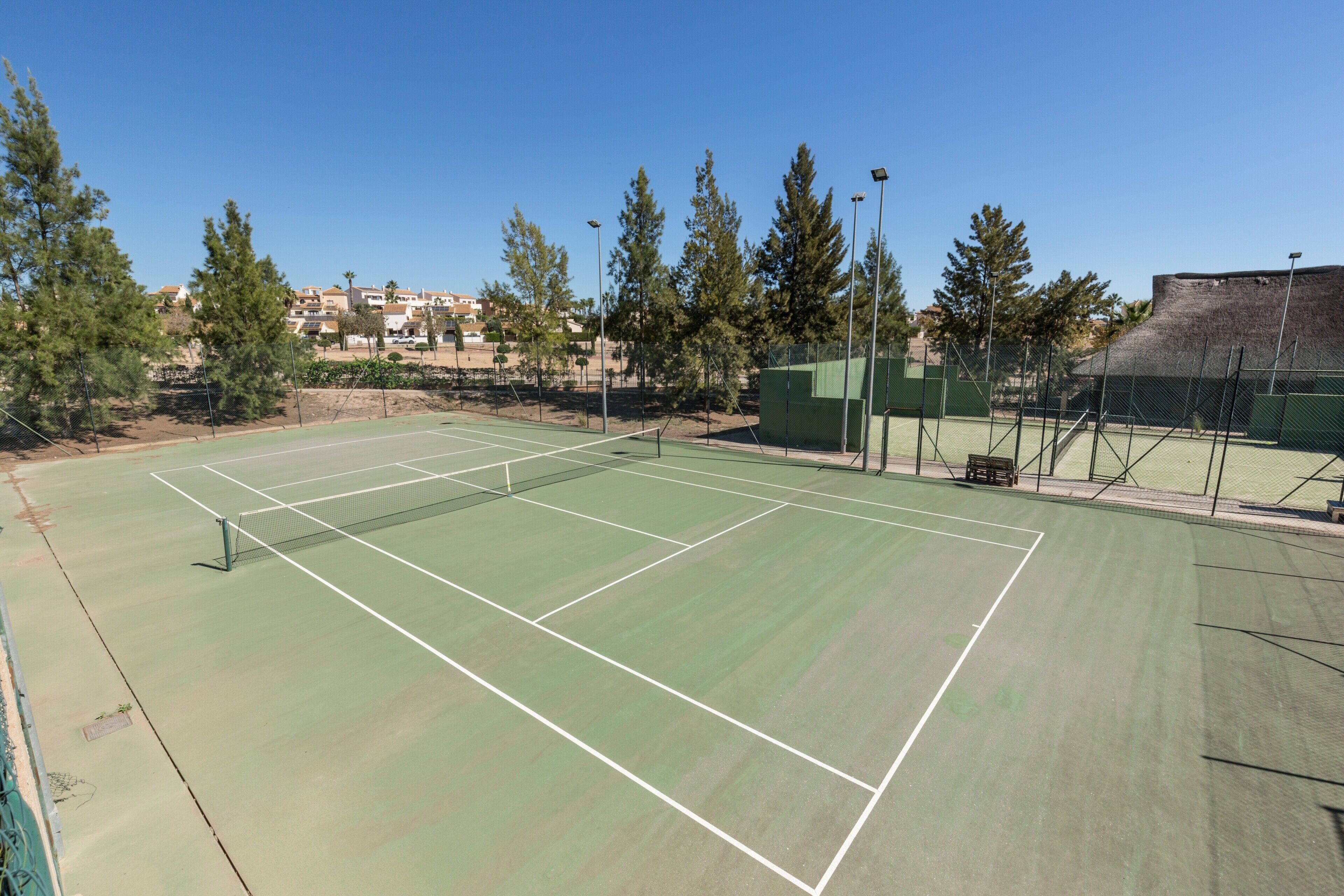 Un campo da tennis con una rete, circondato da alberi e una recinzione.