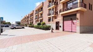 Un edificio residencial de varios pisos con balcones, entrada porticada y un camino peatonal despejado.
