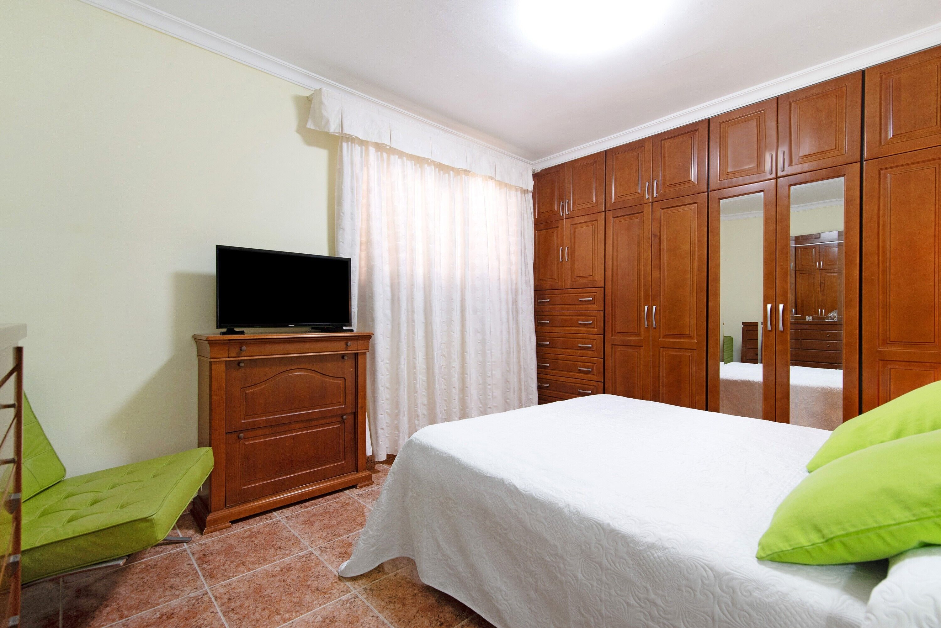 Een slaapkamer met een bed, een televisie op een houten dressoir en een kledingkast.
