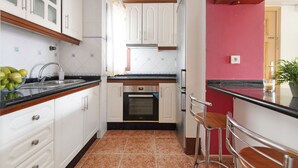 Una cocina con armarios blancos, encimera negra, horno de acero inoxidable y pared roja.