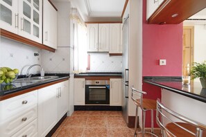 Une cuisine avec des meubles blancs, un plan de travail noir, un four en acier inoxydable et un mur rouge.