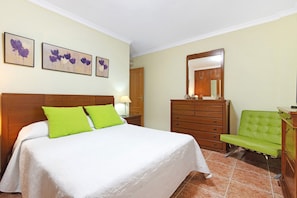 A hotel room with a bed, a green chair, a wooden dresser, and wall art. - Holiday Apartment "Mar Y Sol Salinetas" with Balcony and Garage (Telde)