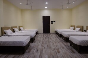 A hotel room with four single beds arranged in a row, a wooden floor, and a door in the center.