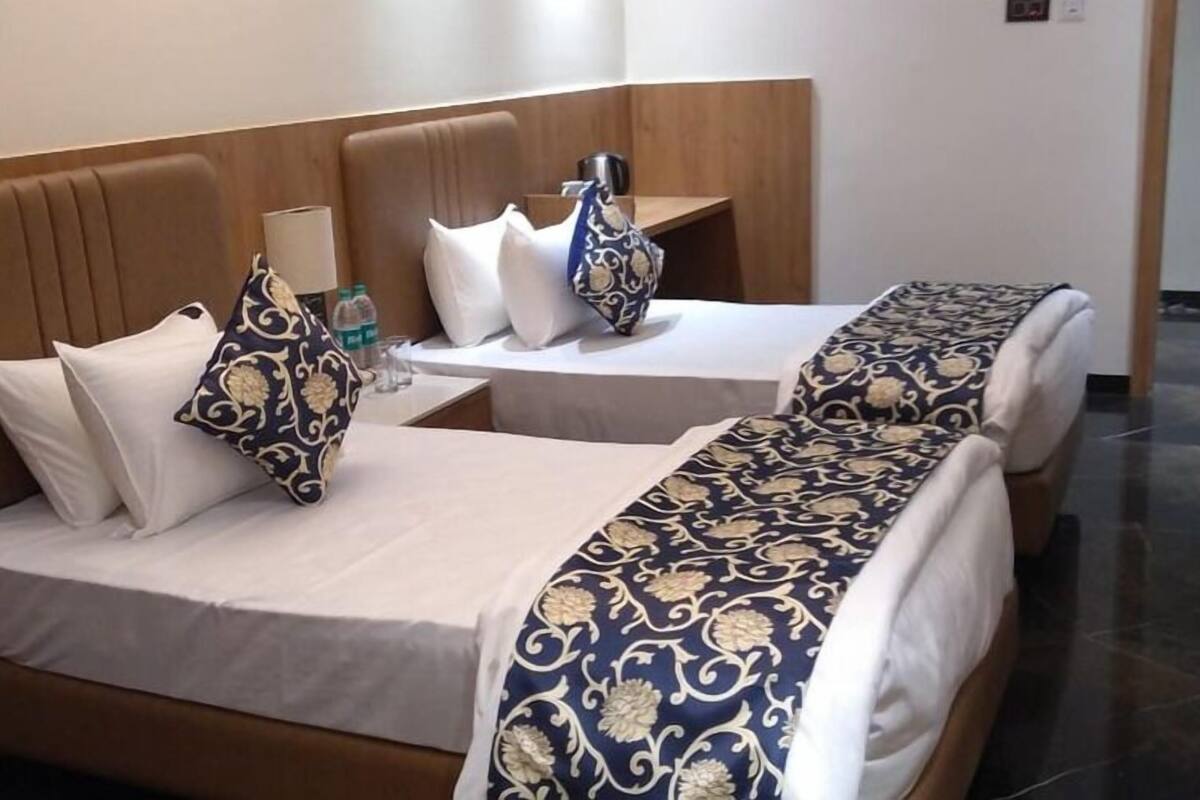 A hotel room with two beds, each with a patterned bedspread and pillows. There is a small table with a bottle and a glass.