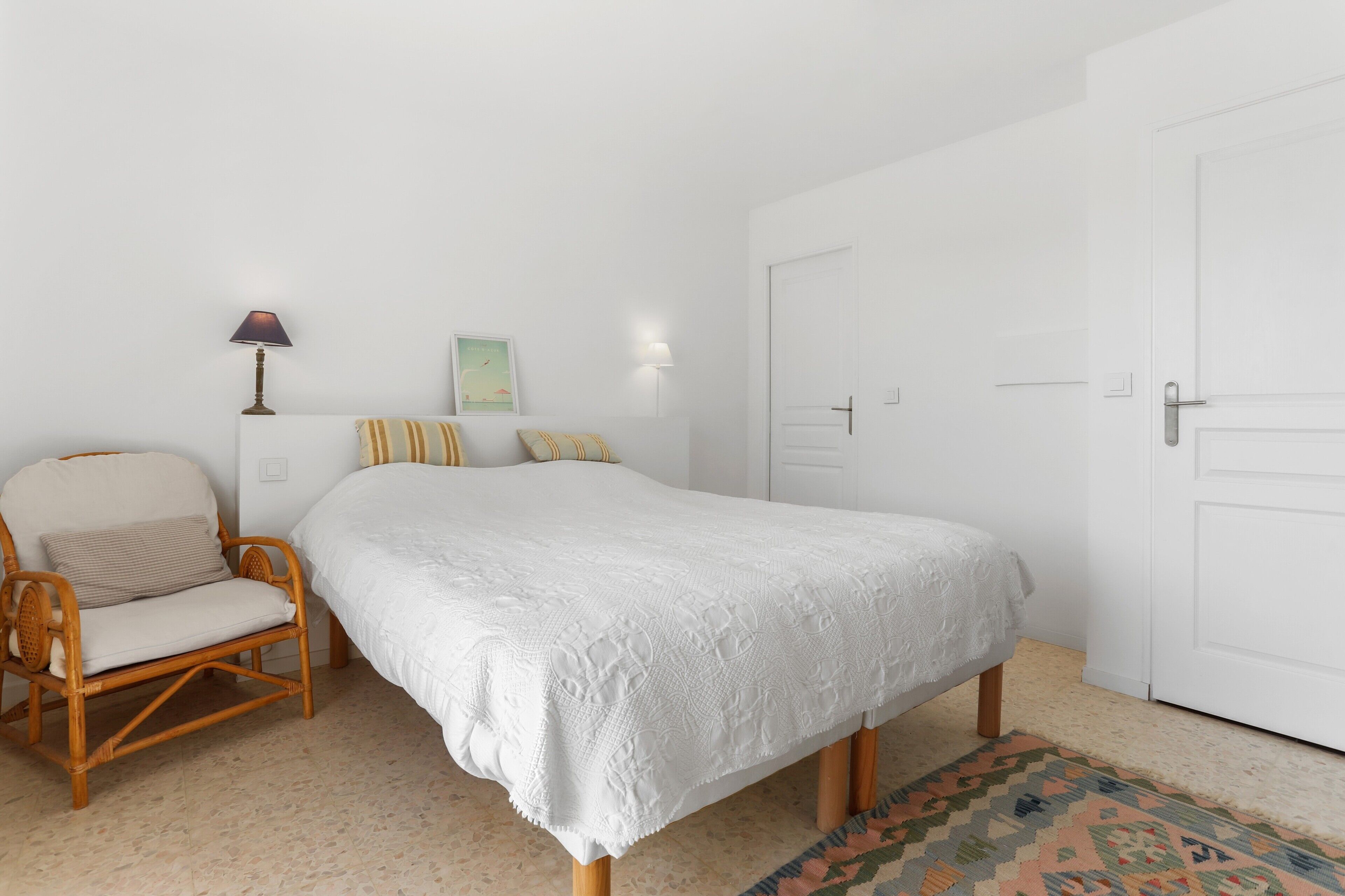 A bedroom with a bed, a chair, a lamp, and a door.