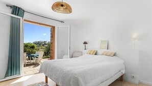 Ein Schlafzimmer mit Bett, Fenster, Tür, Lampe und Blick ins Freie.